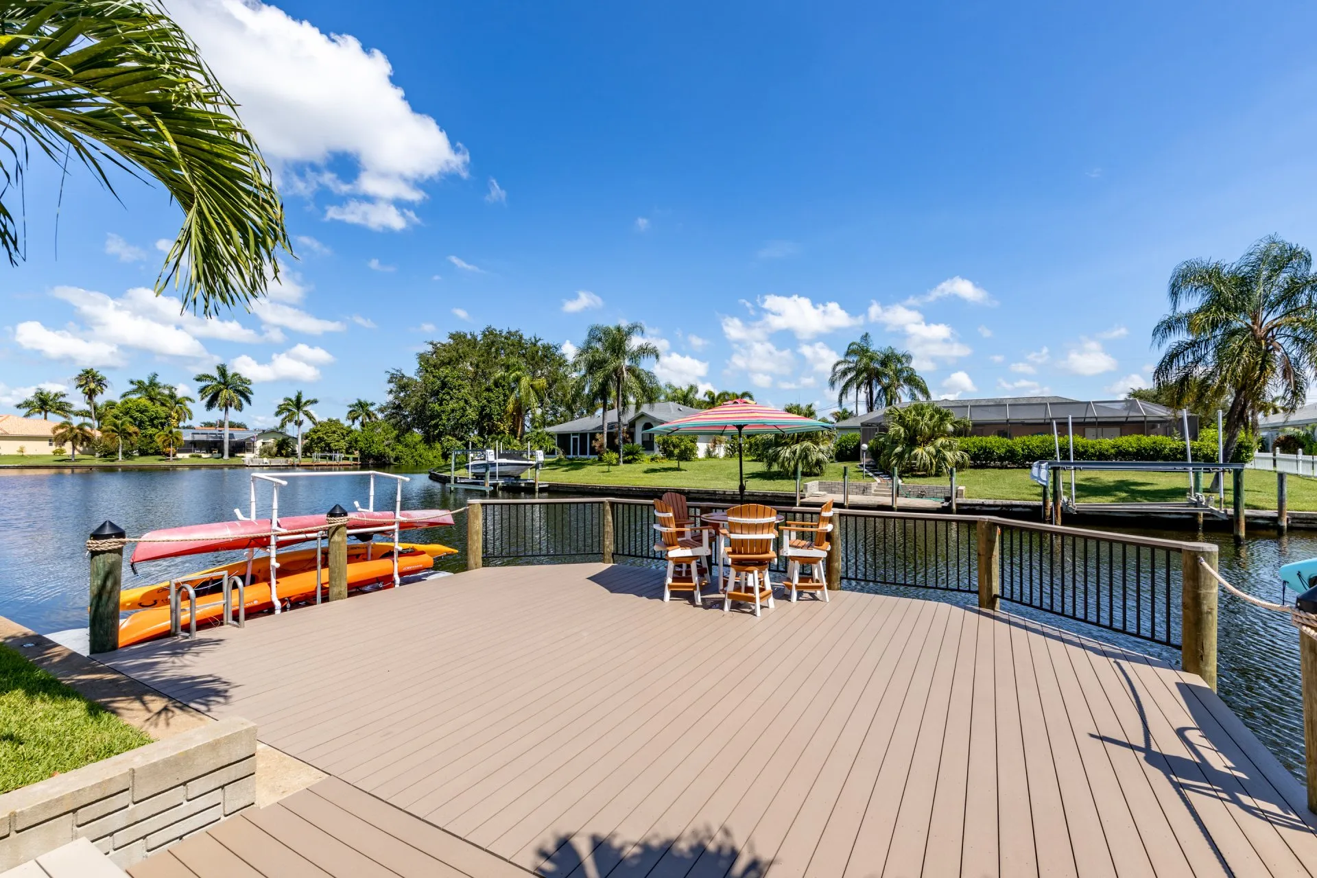 A dock with kayak storage, Adirondack chairs, and a colorful umbrella overlooking a peaceful canal.