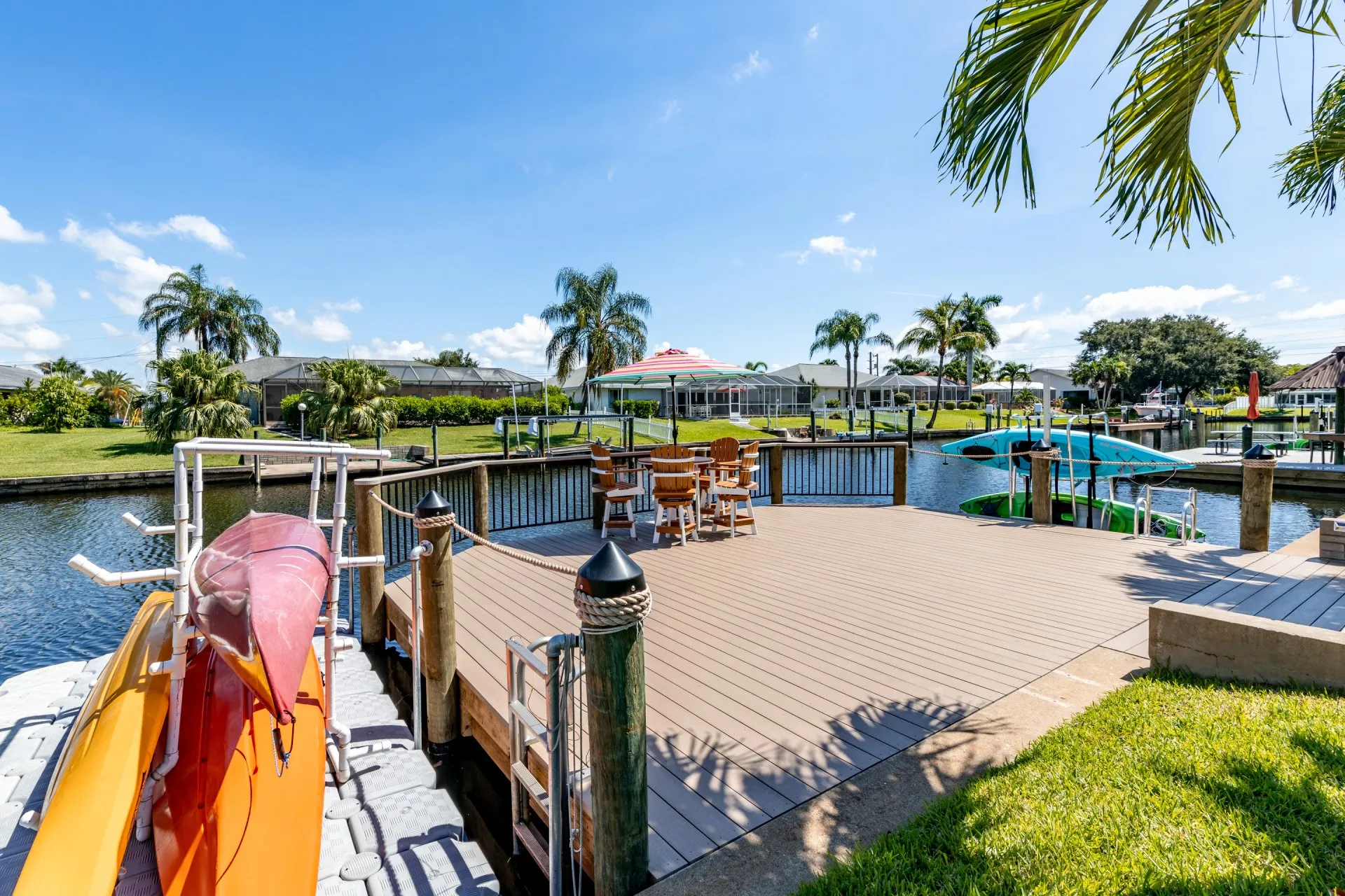 Spacious dock with kayaks and Adirondack seating area featuring a colorful umbrella, set along a scenic canal.