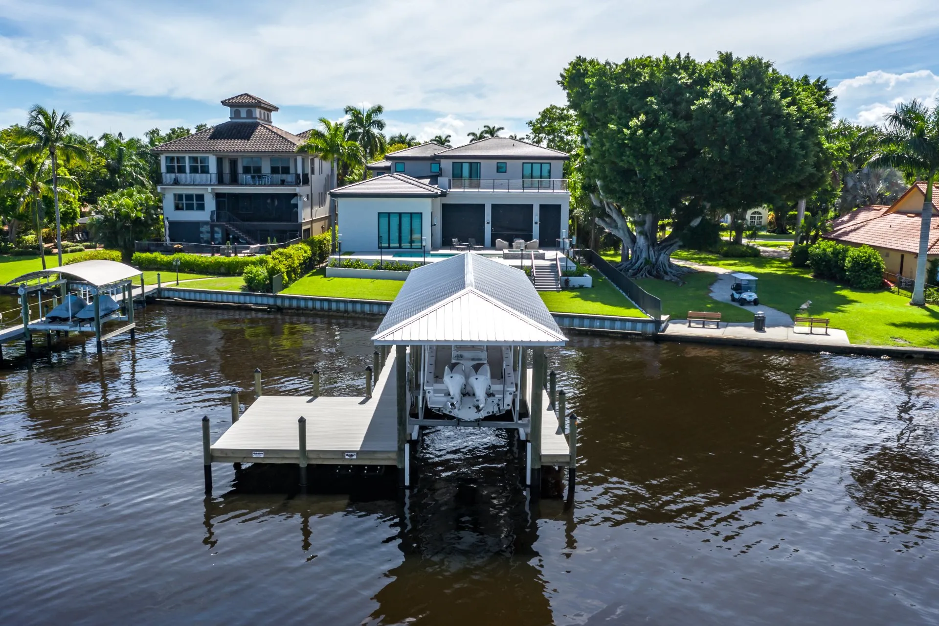 Covered dock with a metal roof and dual-motor boat in front of a modern waterfront home.