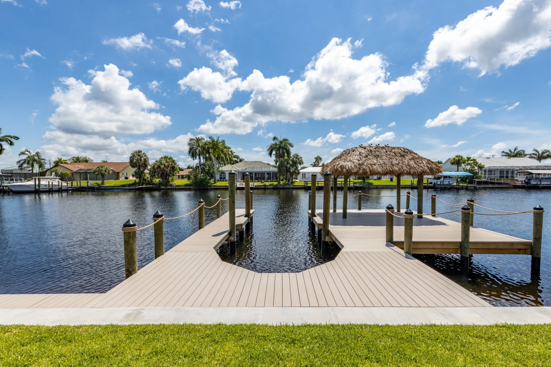 A dock with rope railings and a tiki hut overlooking a calm canal on a sunny day.