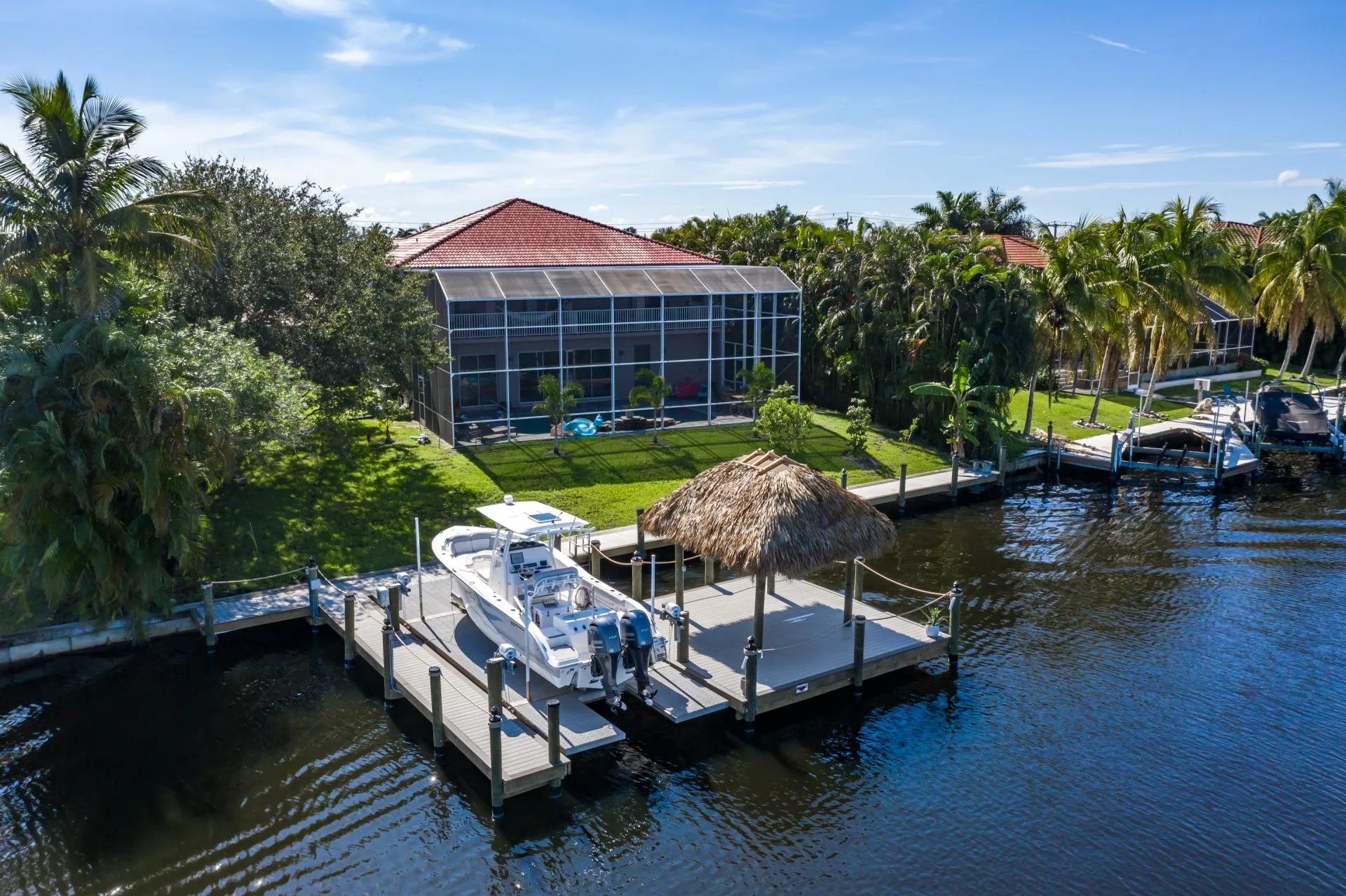 Waterfront property with a docked boat, tiki hut, and lush green yard.