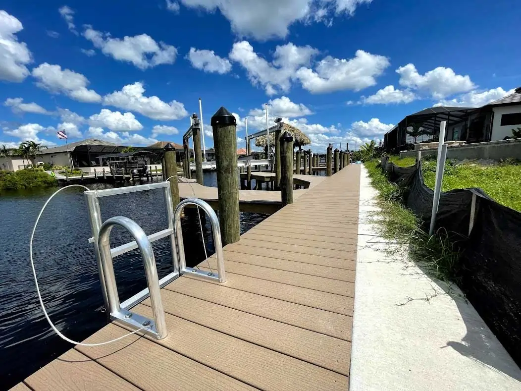 Long wooden dock with a ladder and adjacent walkway under a bright blue sky.