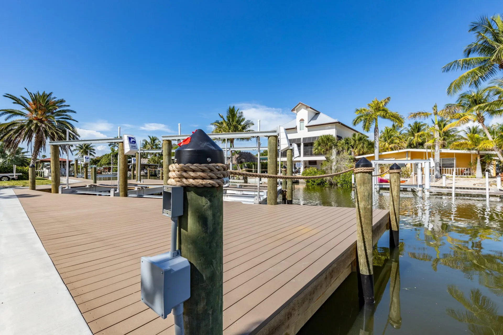 A waterfront dock with wooden pilings, rope accents, and nearby boat lifts under a clear blue sky.