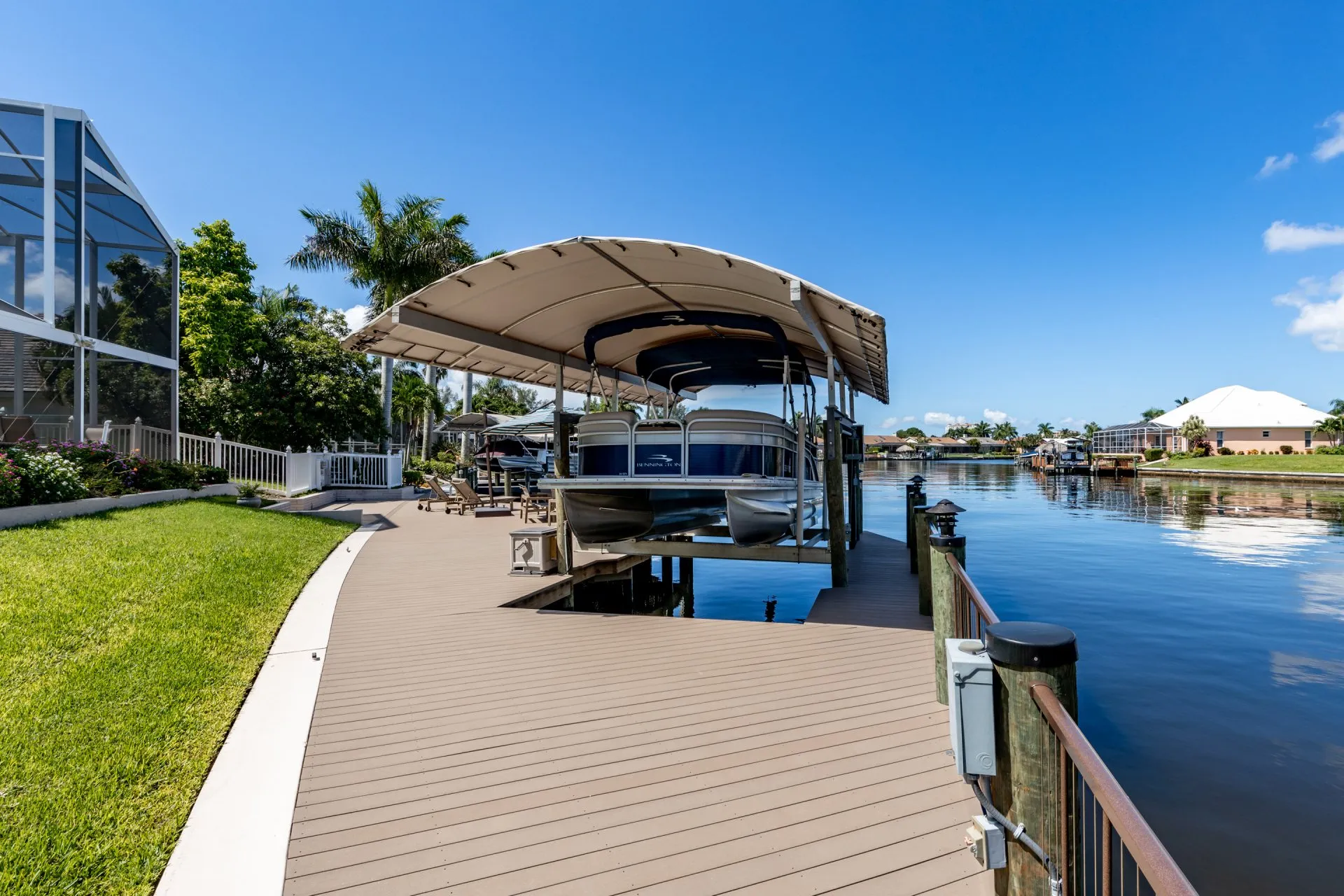 Covered boat lift with a Bennington pontoon along a waterfront dock surrounded by lush greenery.