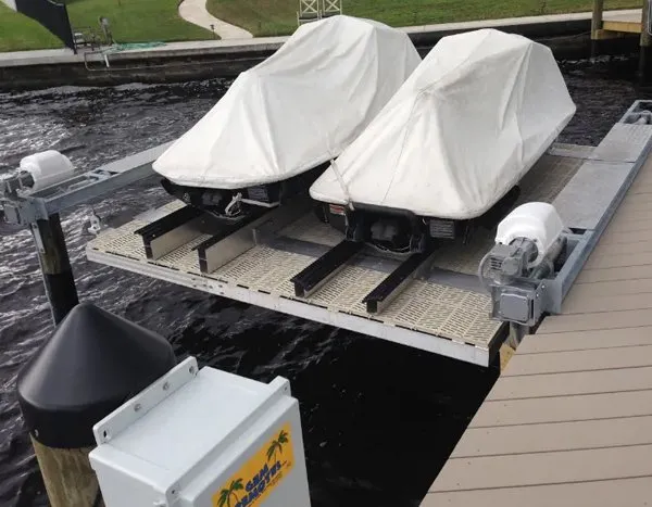 Double jet ski lift with protective covers, motorized controls, and a platform accessory on a dock.