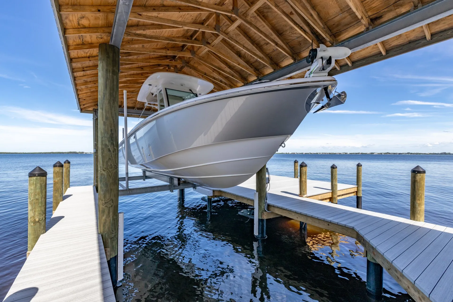 A sleek boat elevated on a lift under a wooden dock shelter, overlooking calm water.