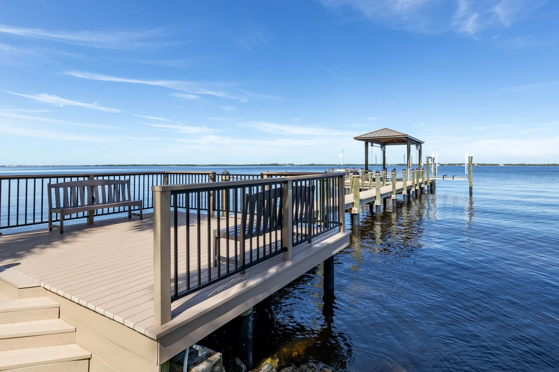 Elevated deck with railing and benches overlooking a dock and serene waterfront.