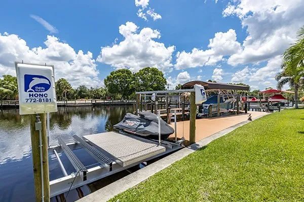 A canal-side dock with a jet ski lift and boat lift, featuring a green lawn and a sunny residential backdrop.