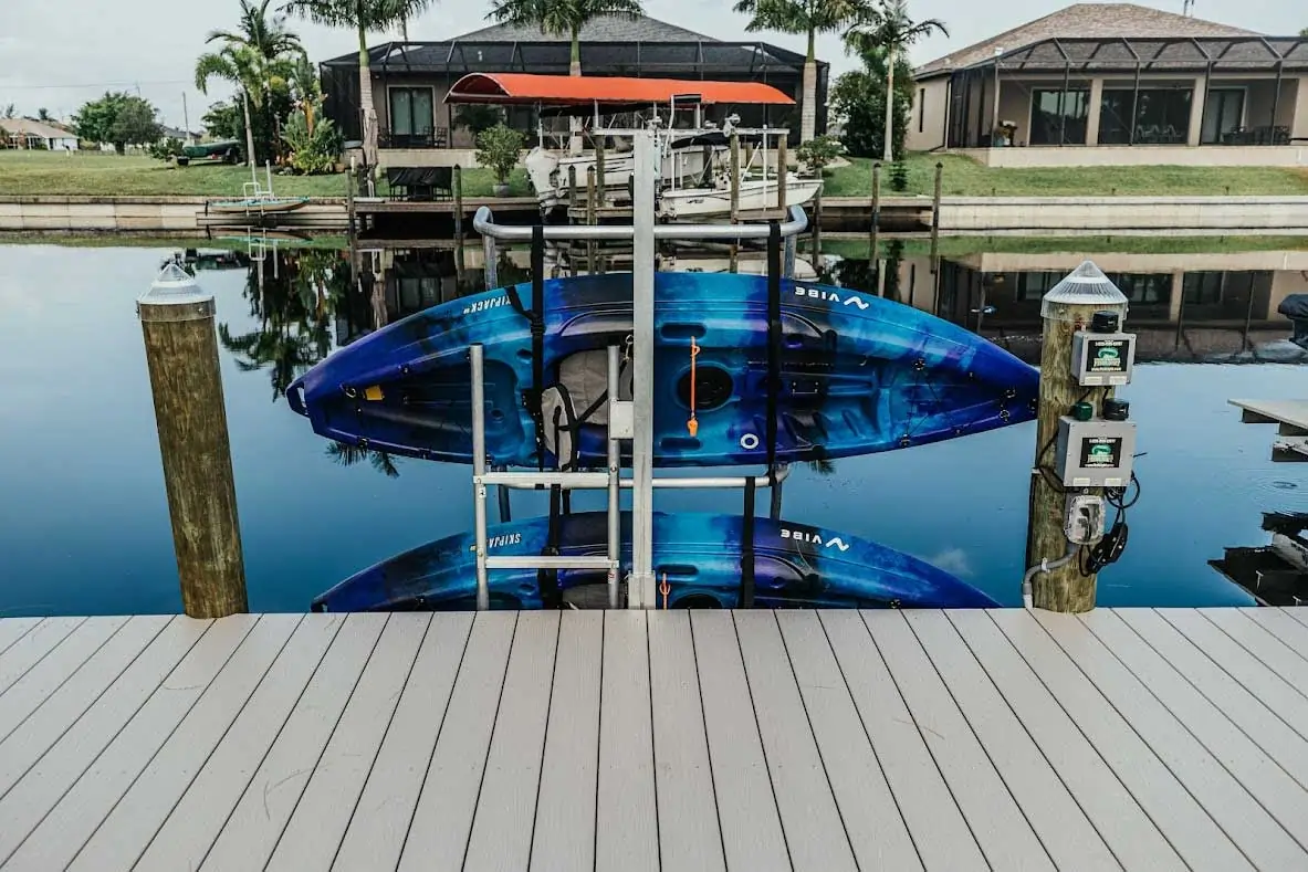 Two blue kayaks stored vertically on a dock lift with calm water reflecting their image.