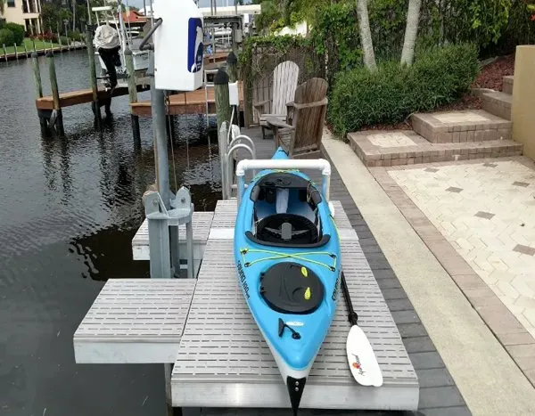 Blue kayak placed on a kayak launch platform attached to a dock, with a paddle resting nearby.