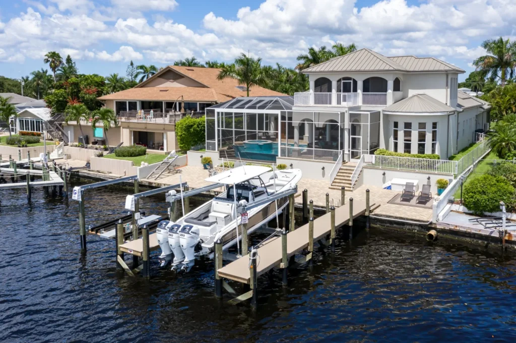 Waterfront home with a screened pool, large dock, and boat lift featuring triple outboard motors.