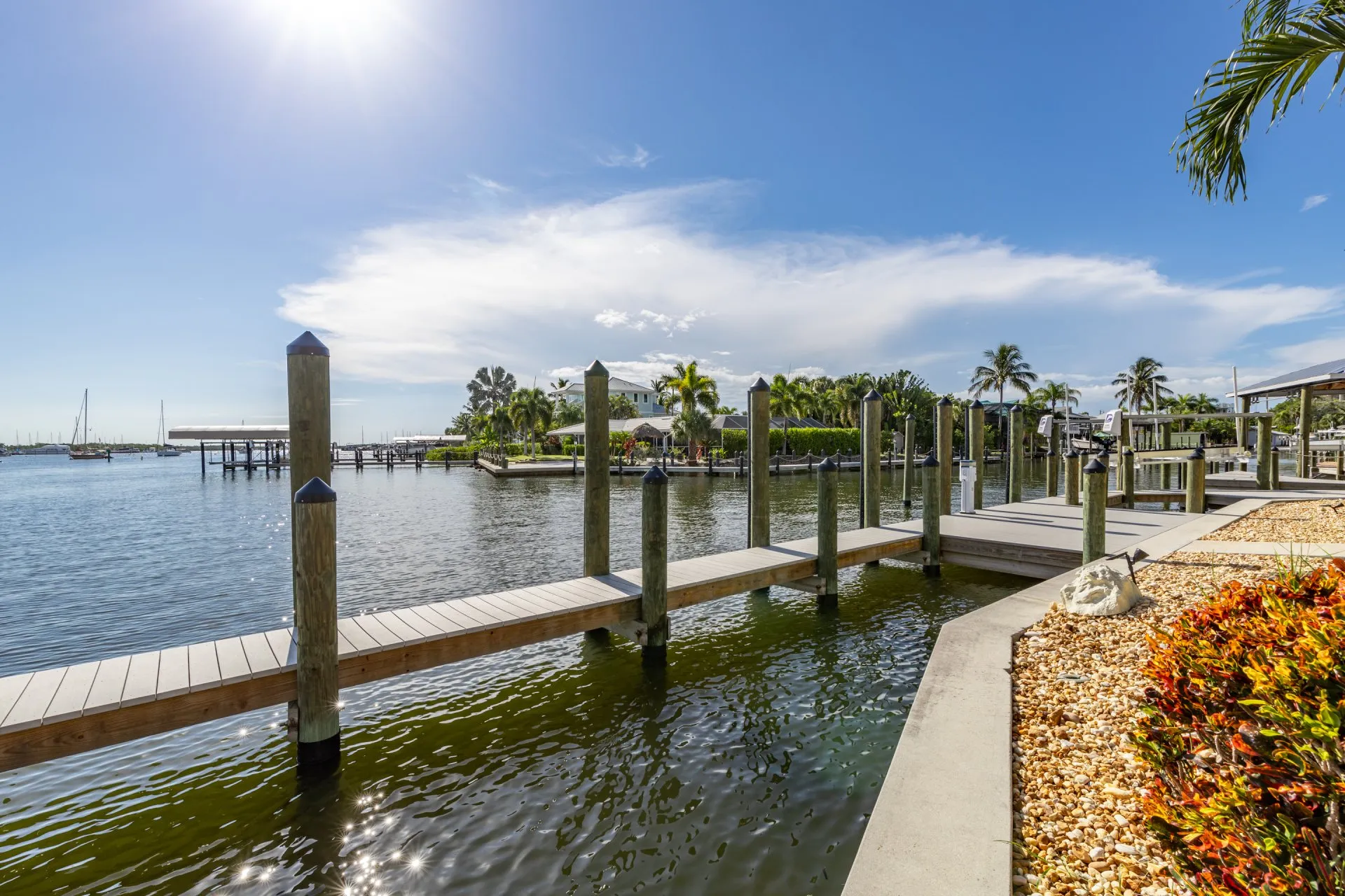 Modern waterfront dock featuring wooden walkways, mooring posts, and a landscaped shoreline under a bright sunny sky.