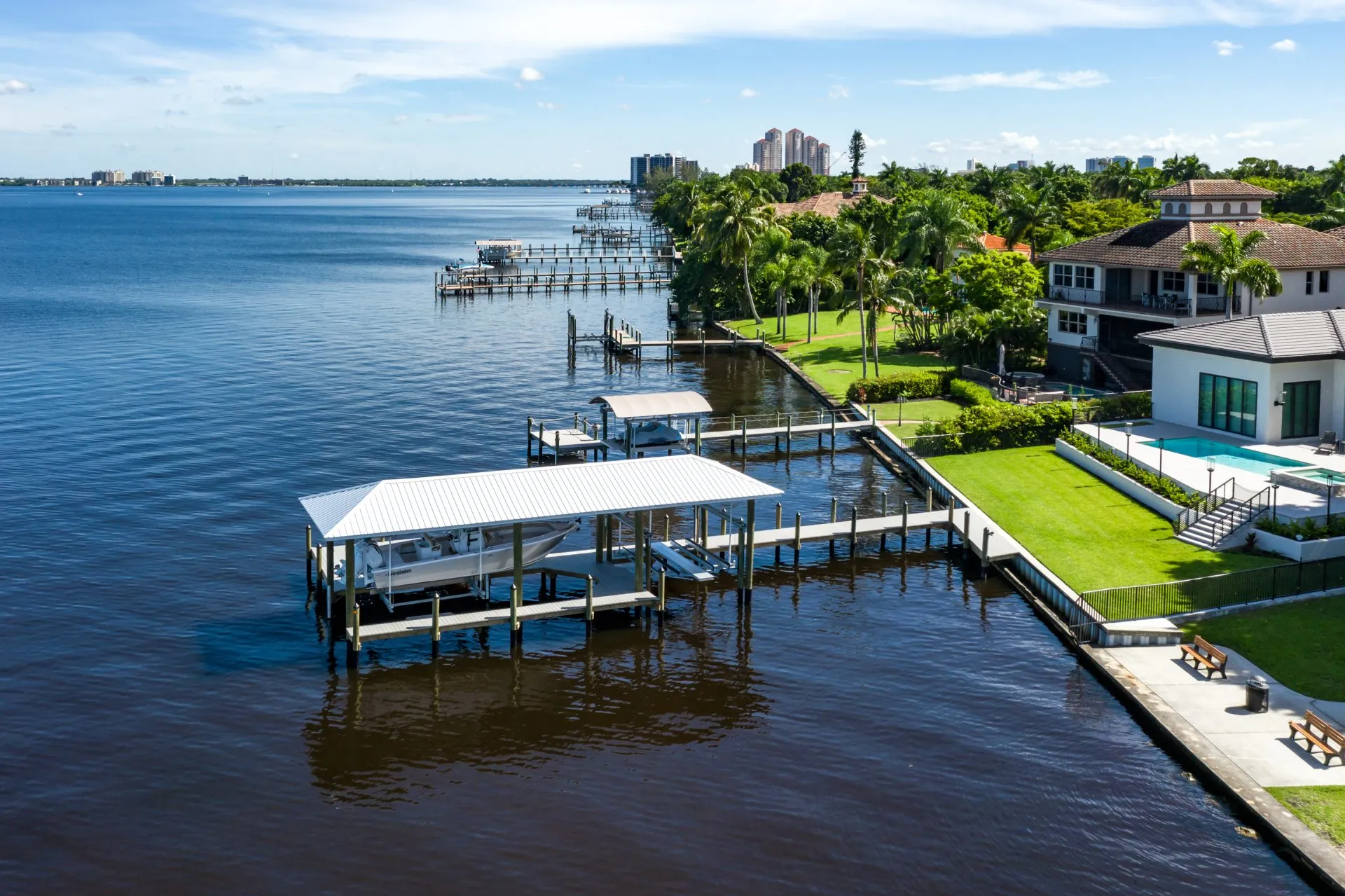 A modern dock with a boat lift and scenic waterfront homes in a tropical setting.