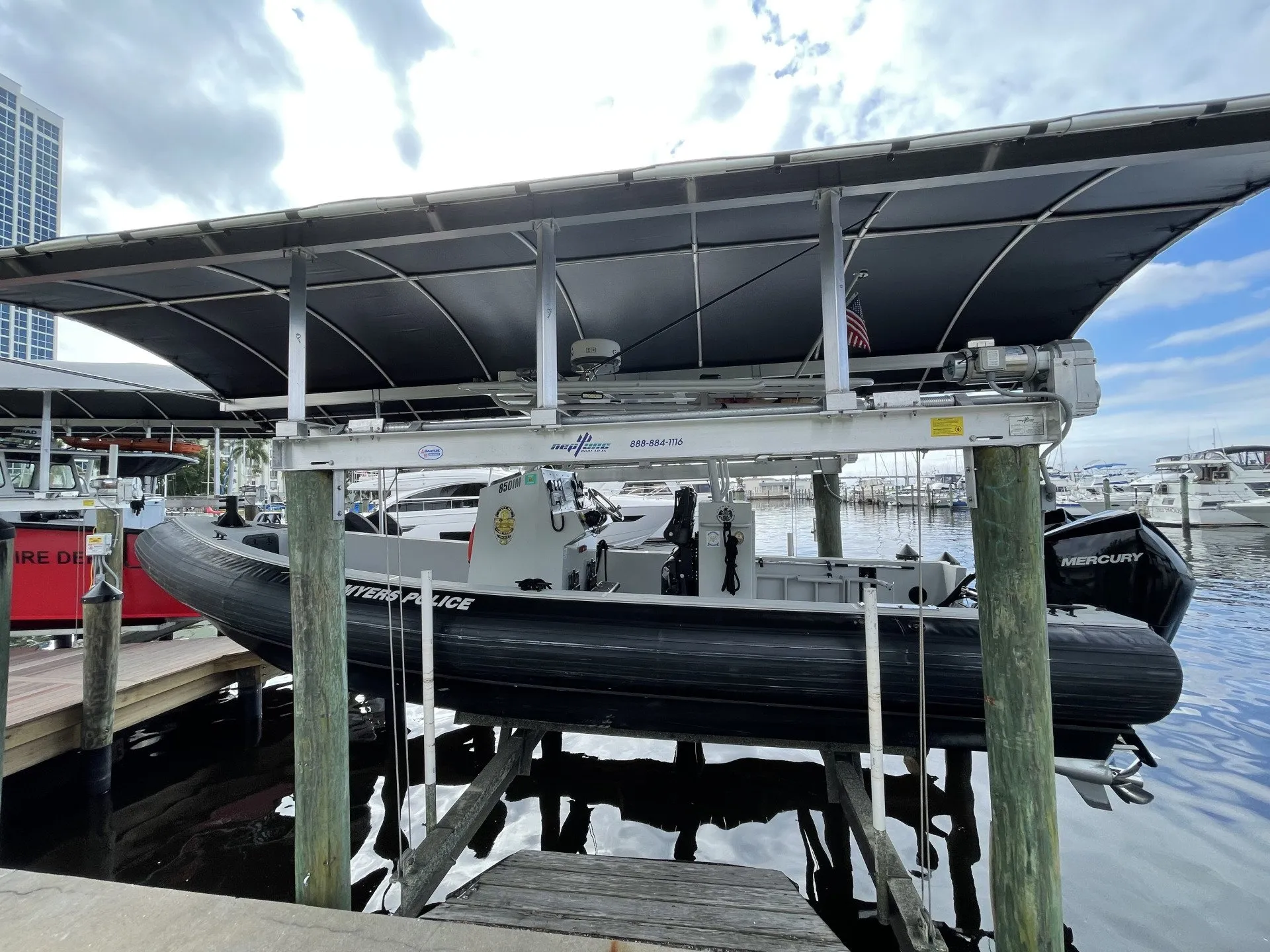 A Fort Myers Police boat on a custom lift under a covered dock in a marina.