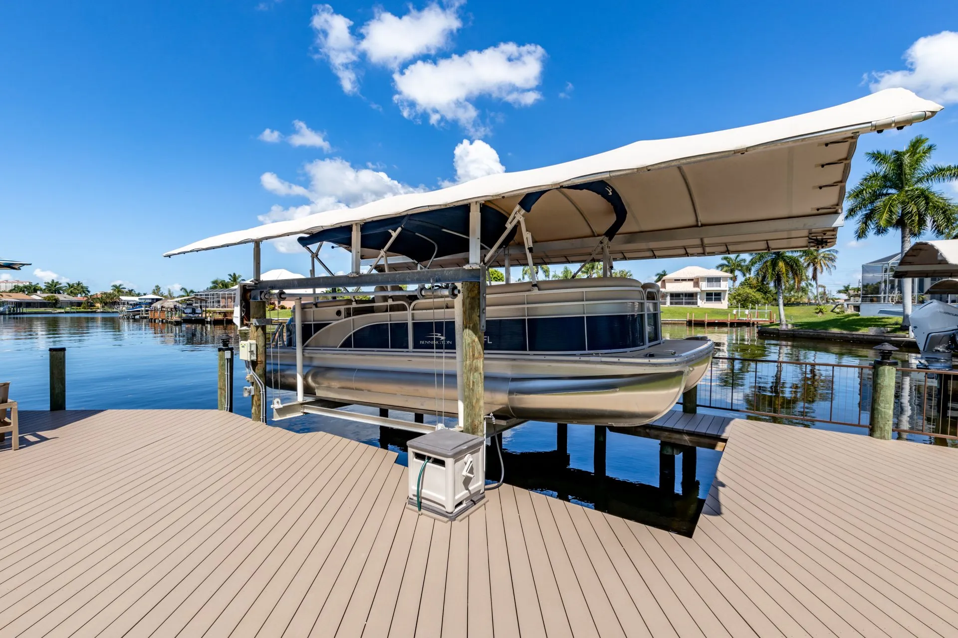 Pontoon boat docked under a canopy on a wooden waterfront deck with scenic canal views.