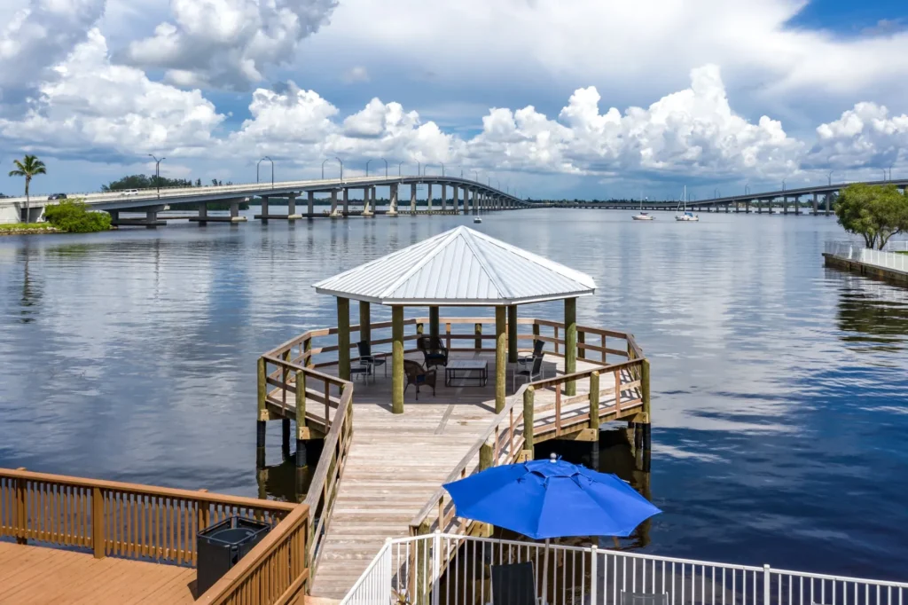 Riverside pavilion with a metal roof, overlooking a scenic bridge and calm water.