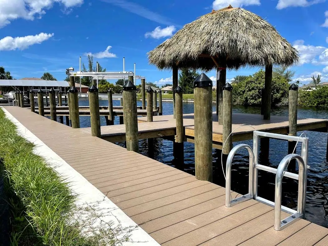 Wooden dock with a ladder and tiki hut surrounded by calm water and a blue sky.