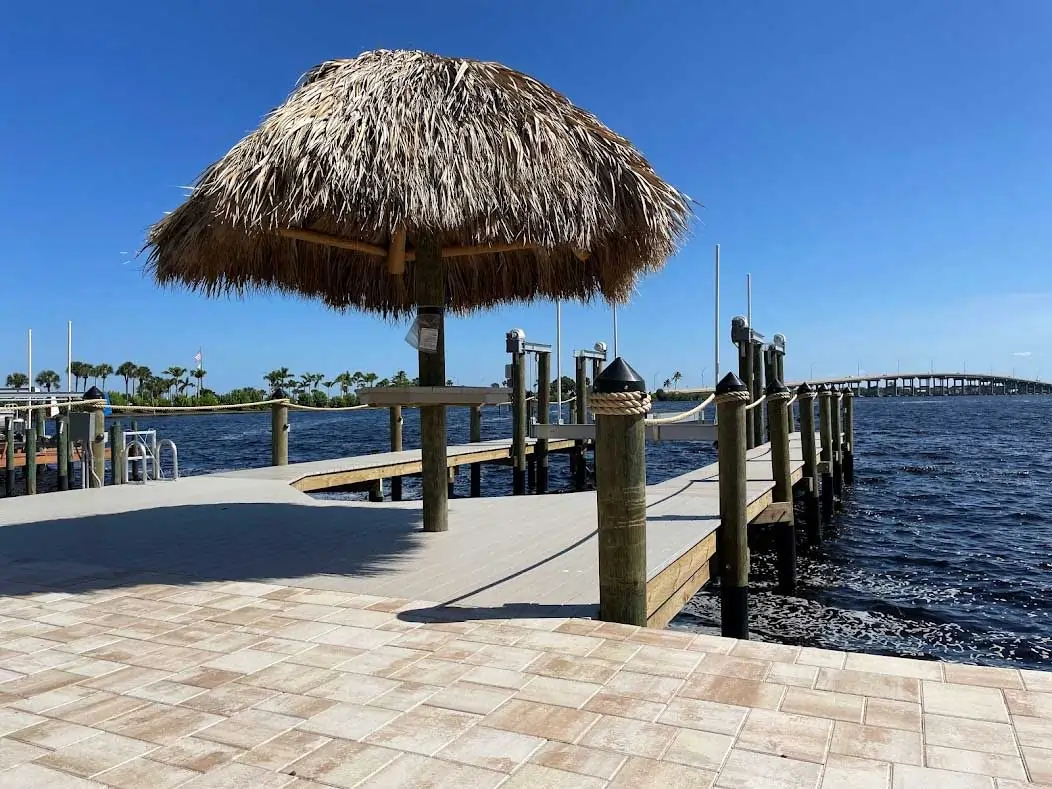 A dock with a tiki hut overlooking the water, with a bridge visible in the distance under a clear blue sky.