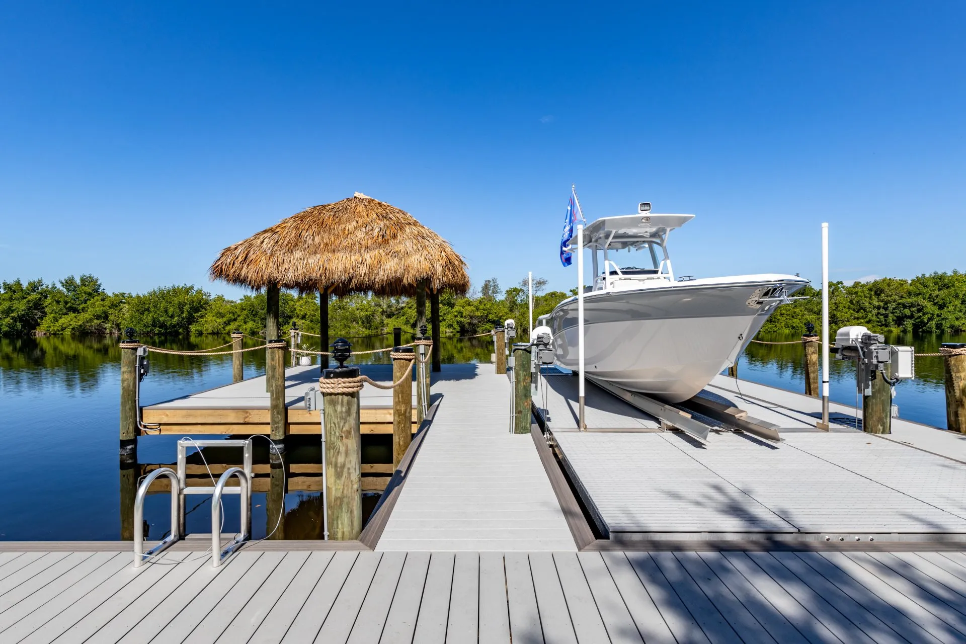 A modern dock with a thatched tiki hut and a large white boat under a clear blue sky.