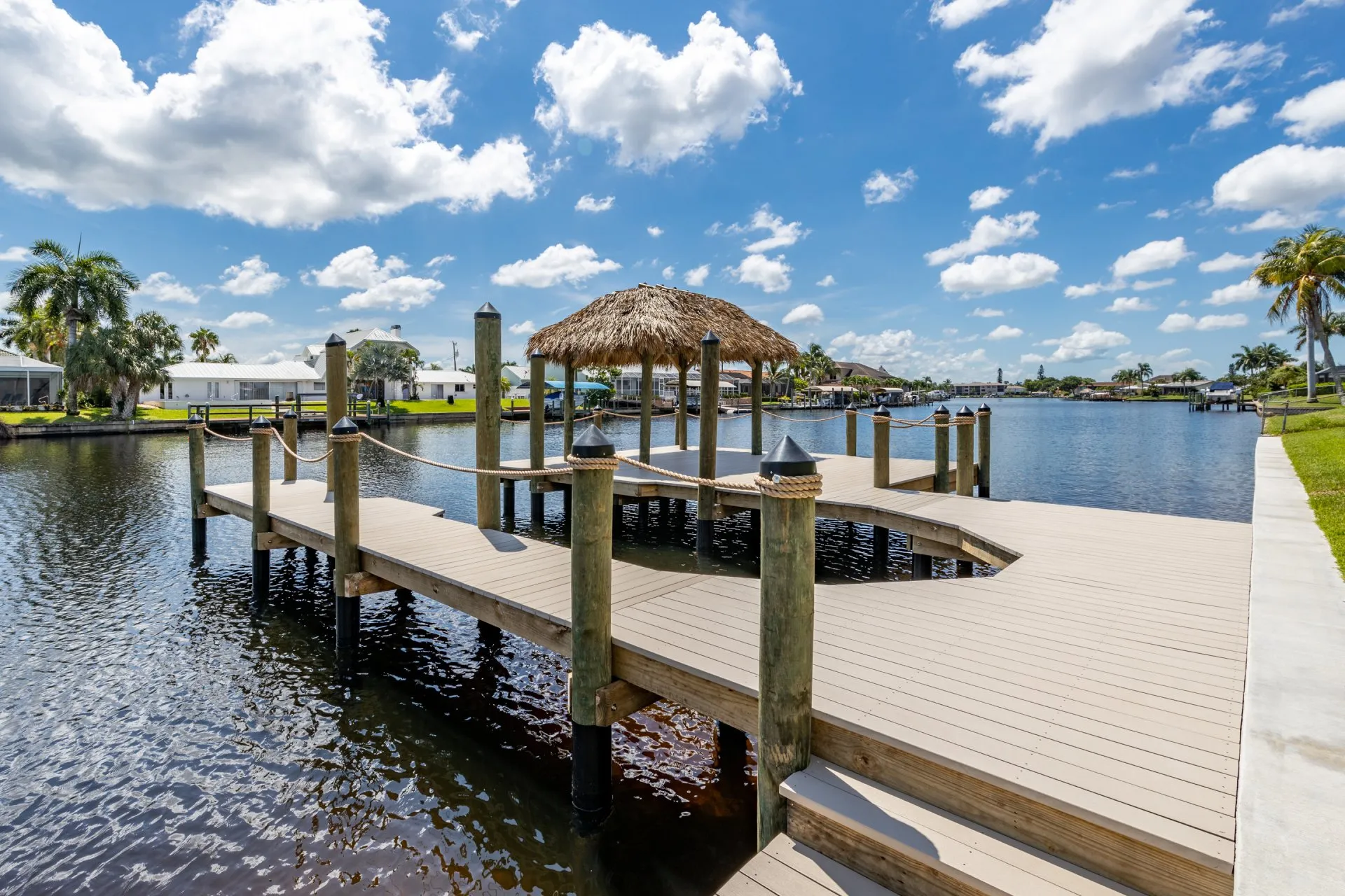 A waterfront dock with a tiki hut surrounded by a calm canal and clear blue skies.