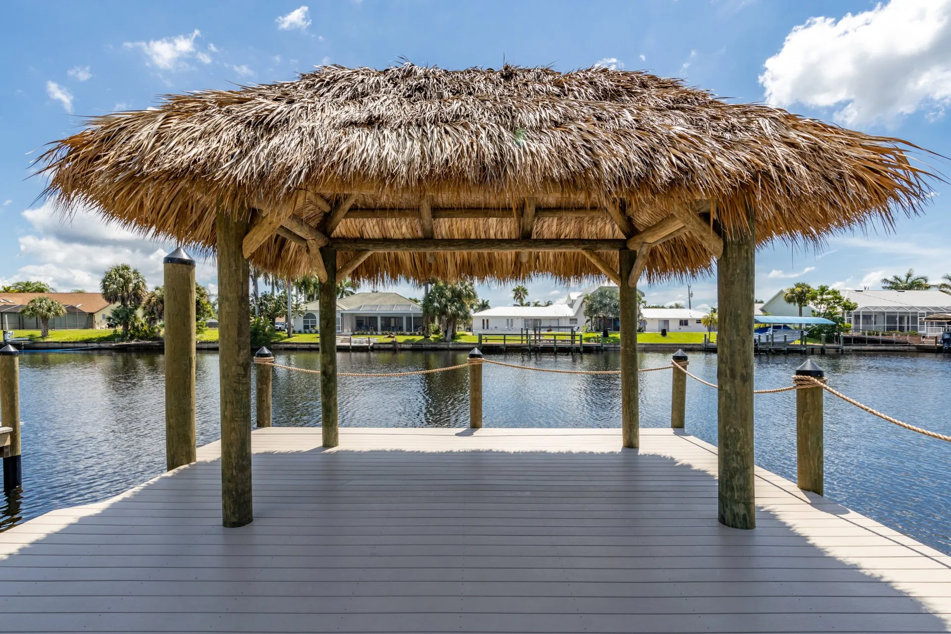 Close-up view of a tiki hut on a dock with rope railings, overlooking a calm canal.