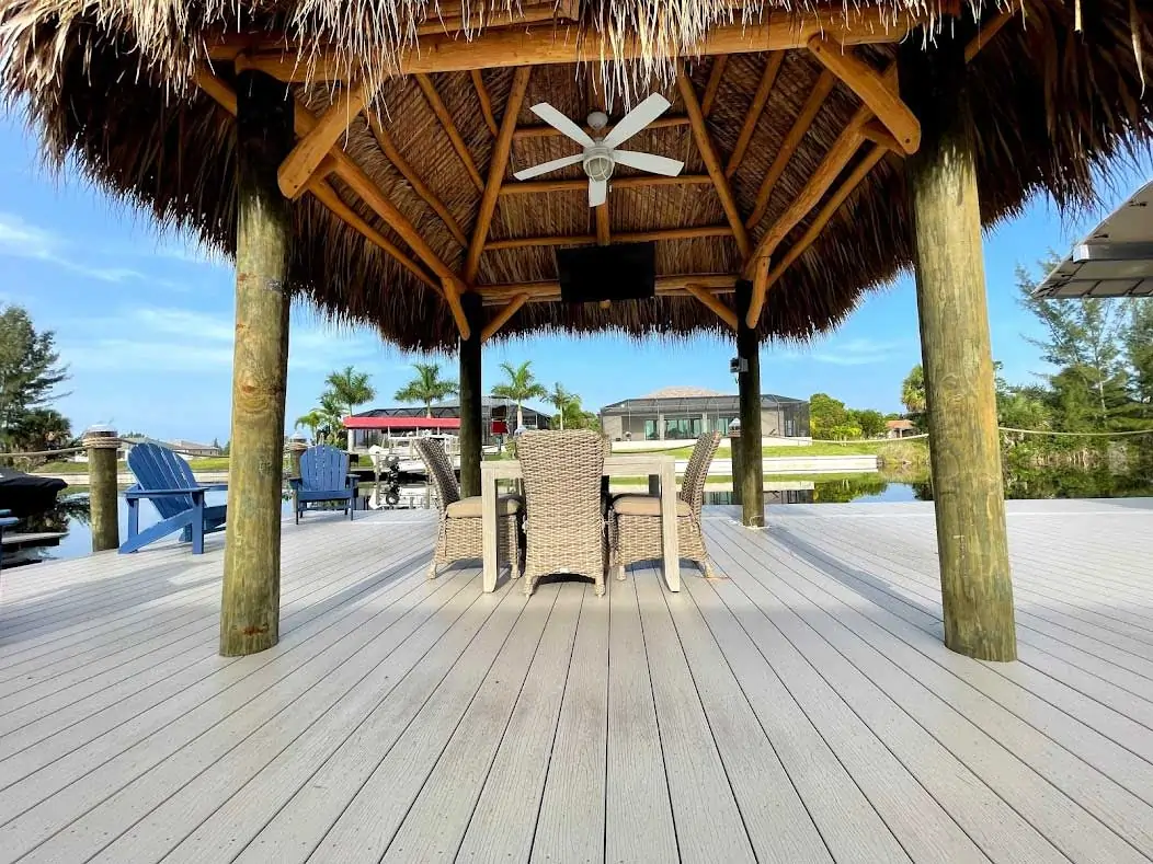 Tiki hut with a ceiling fan, chairs, and table on a dock with composite decking.