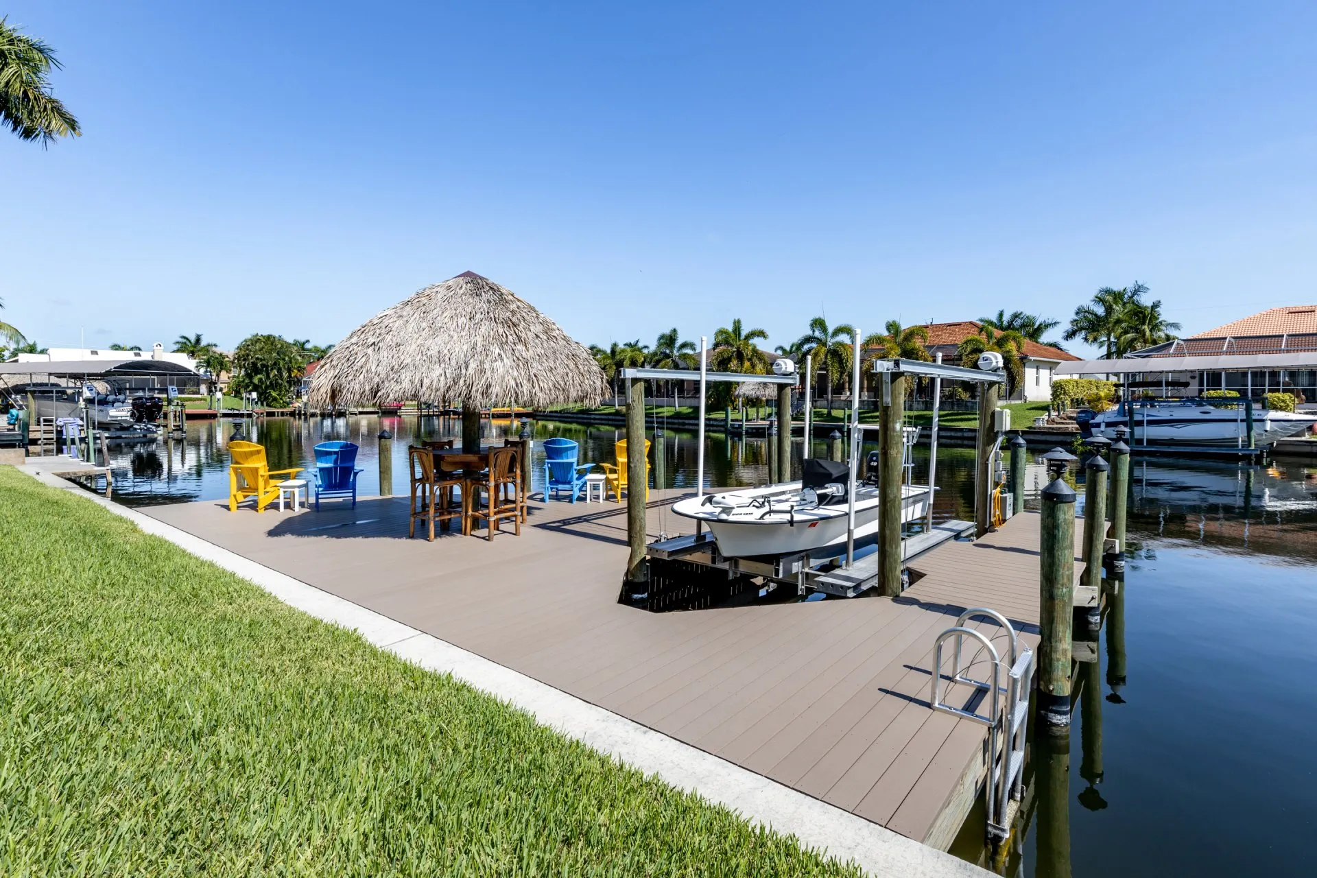 Dock with a tiki hut, colorful chairs, and a boat lift in a canal setting.