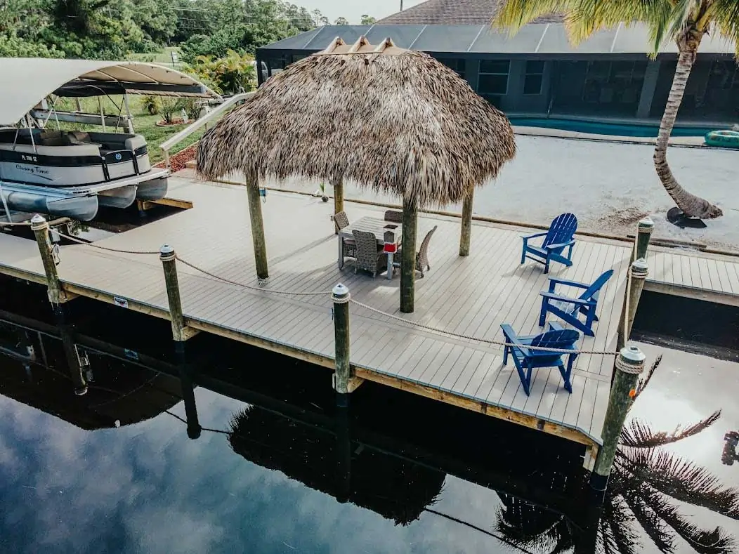 Dock with a tiki hut, lounge chairs, and a covered pontoon boat on a calm waterfront.