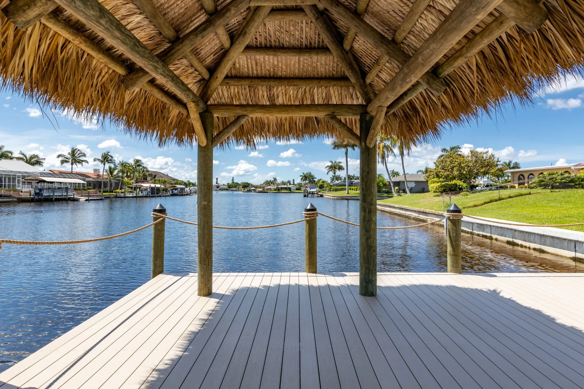 View from a tiki hut on a dock overlooking a scenic canal and waterfront homes.