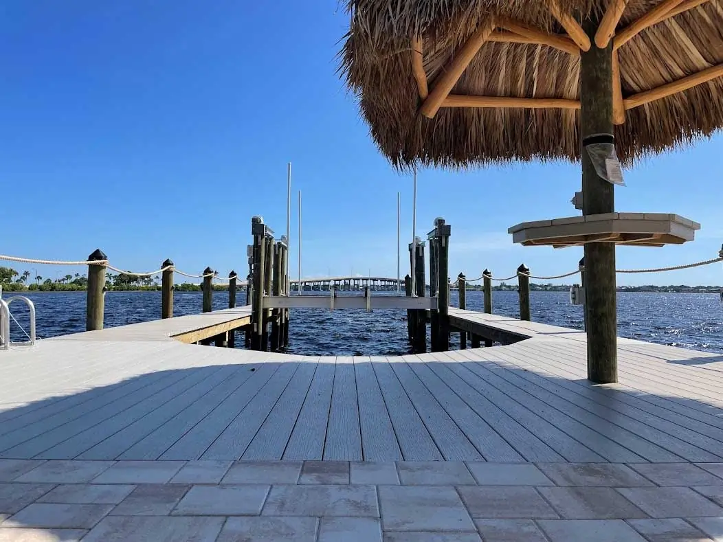 Tiki hut overlooking a white wooden dock extending into a calm waterfront with clear blue skies.