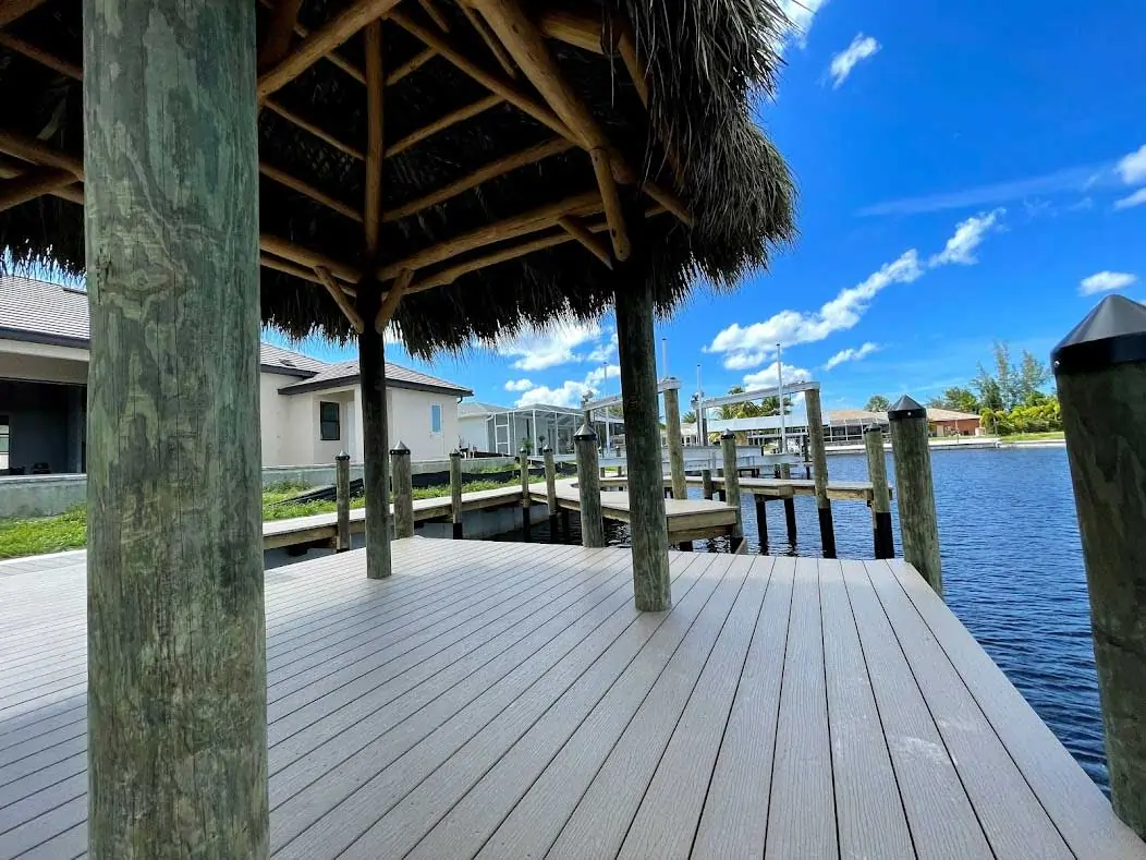 Close-up of a wooden dock under a tiki hut overlooking the water with pilings and clear blue skies.