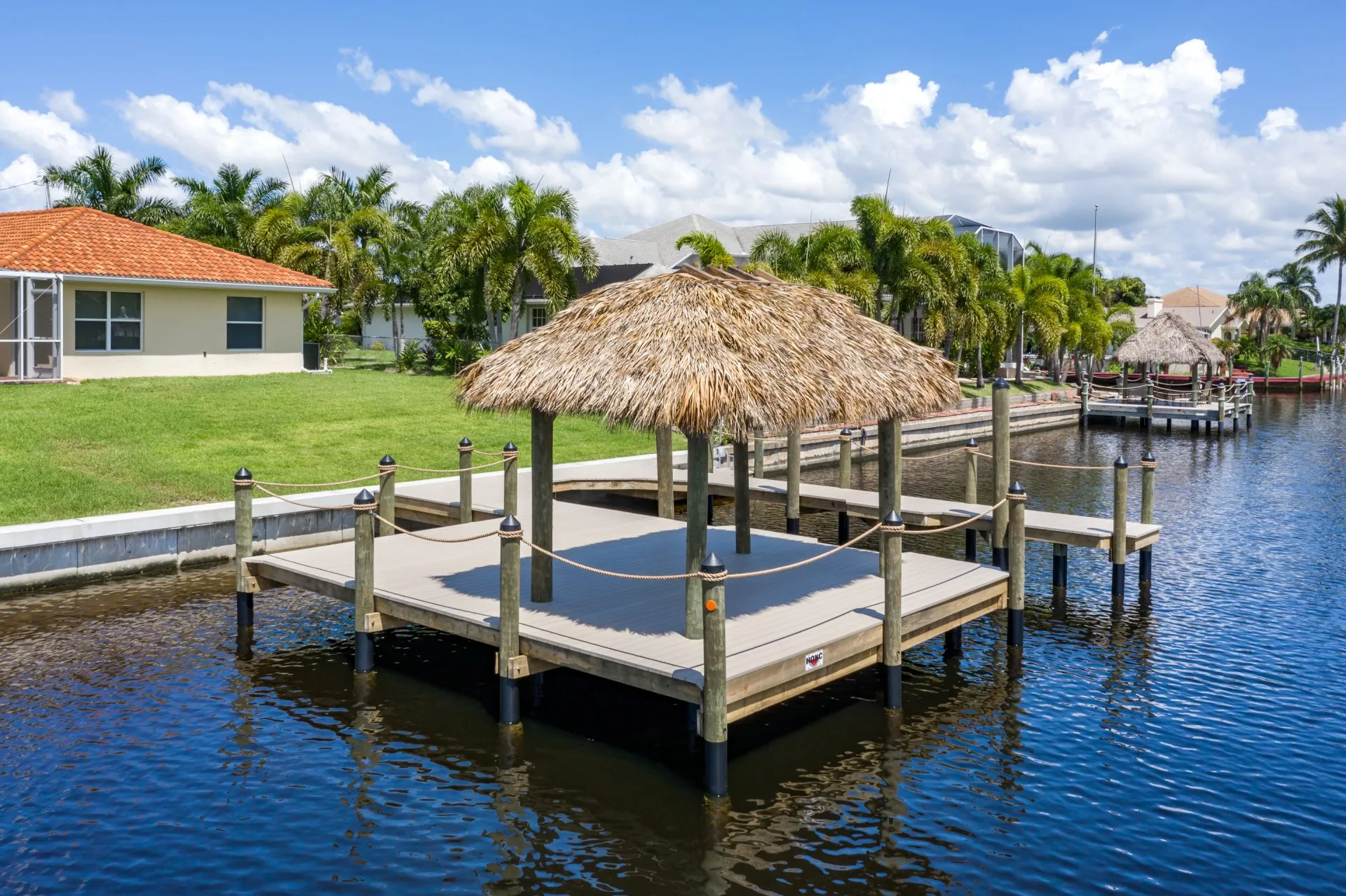 Waterfront dock with a tiki hut surrounded by calm water and a green backyard.