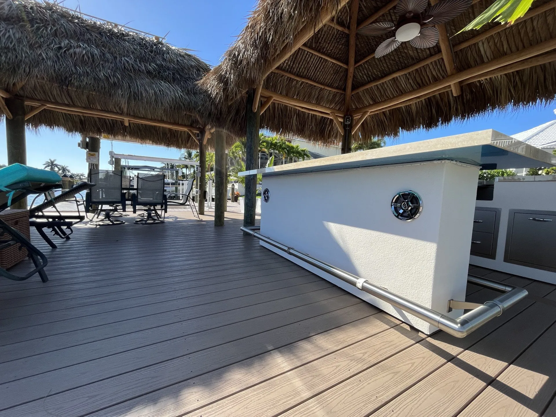 A tiki hut featuring a modern bar setup with seating, lounge chairs, and a waterfront view.