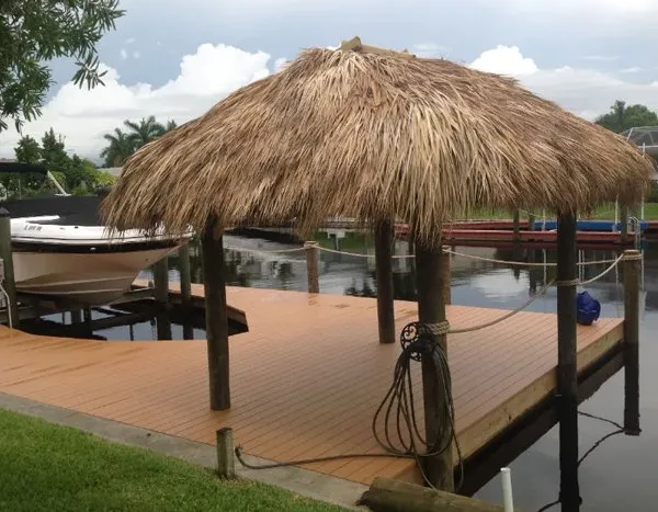 Tiki hut with a thatched roof on a wooden dock, providing shade near a boat on a calm canal.