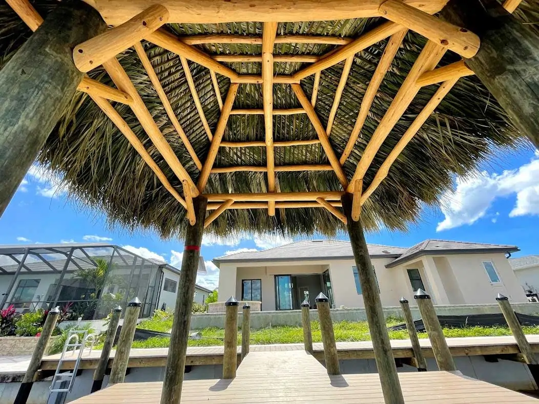 Underside view of a tiki hut showcasing wooden beams and thatched roof on a waterfront dock.