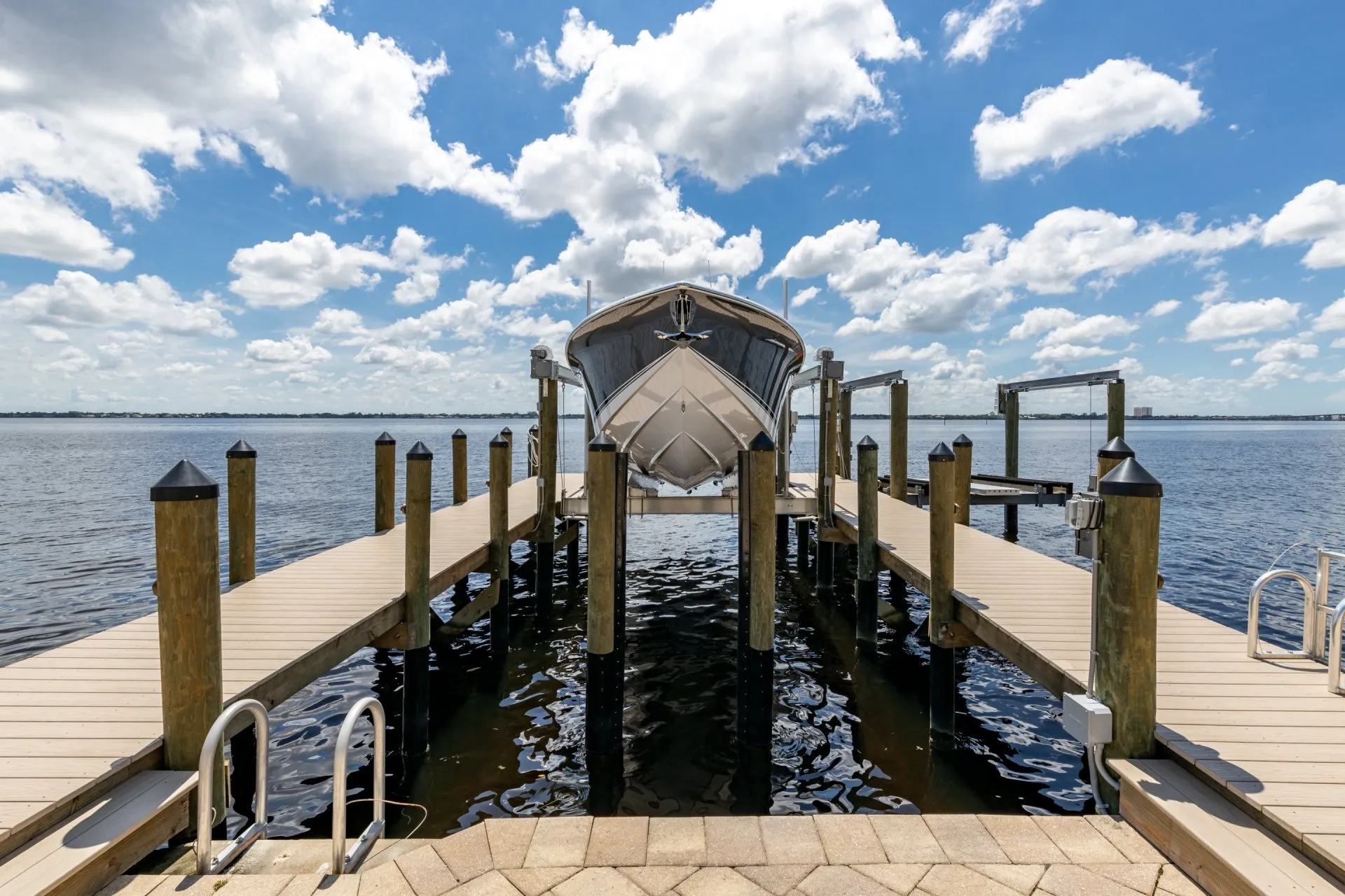 A boat lifted on a dock overlooking a serene waterfront with a bright blue sky and scattered clouds.