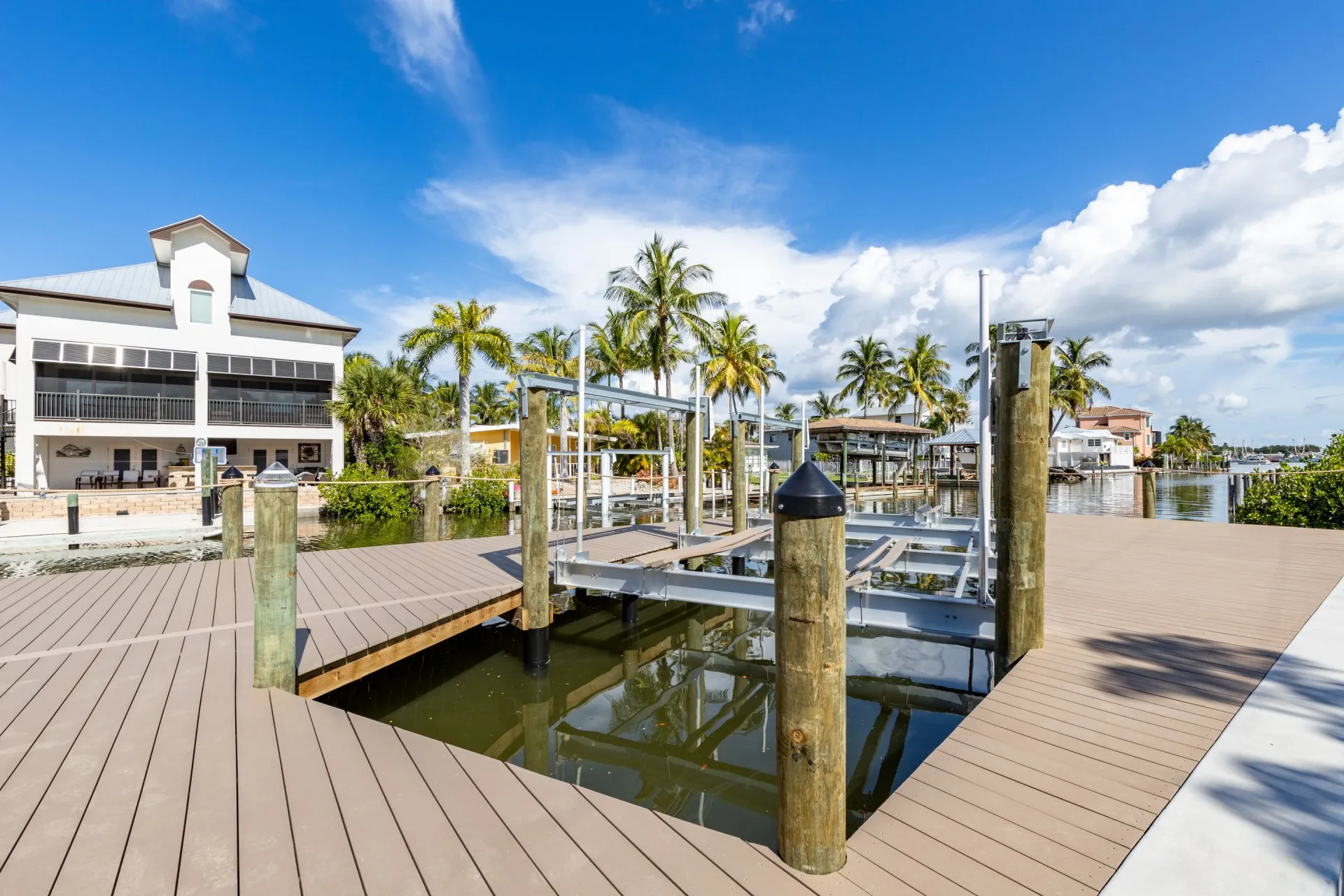 A newly installed boat lift on a modern dock by a canal, surrounded by tropical homes and palm trees.