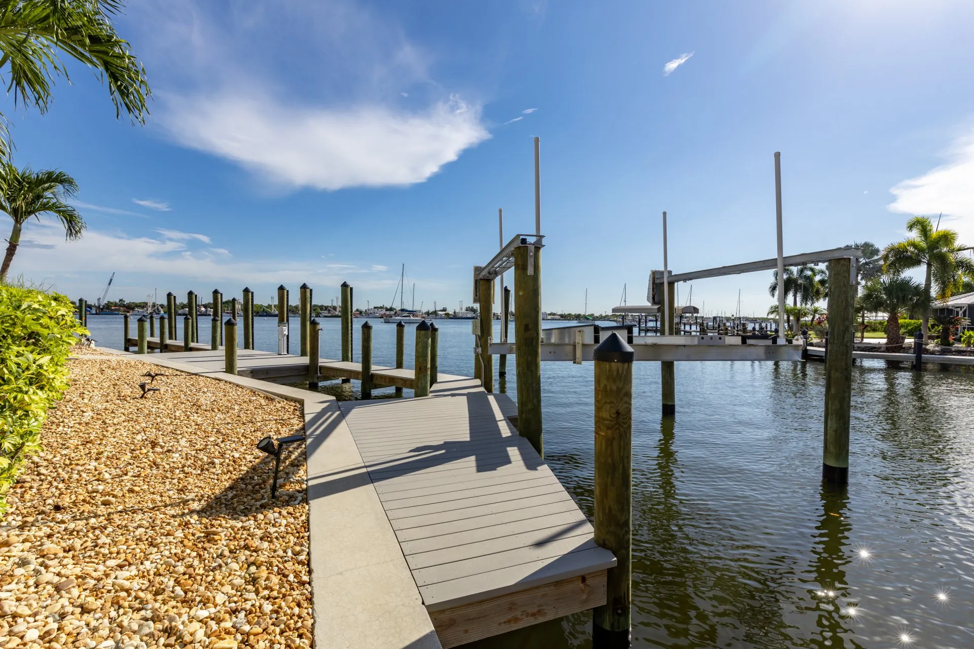 Waterfront dock with boat lift and pilings under a bright blue sky.