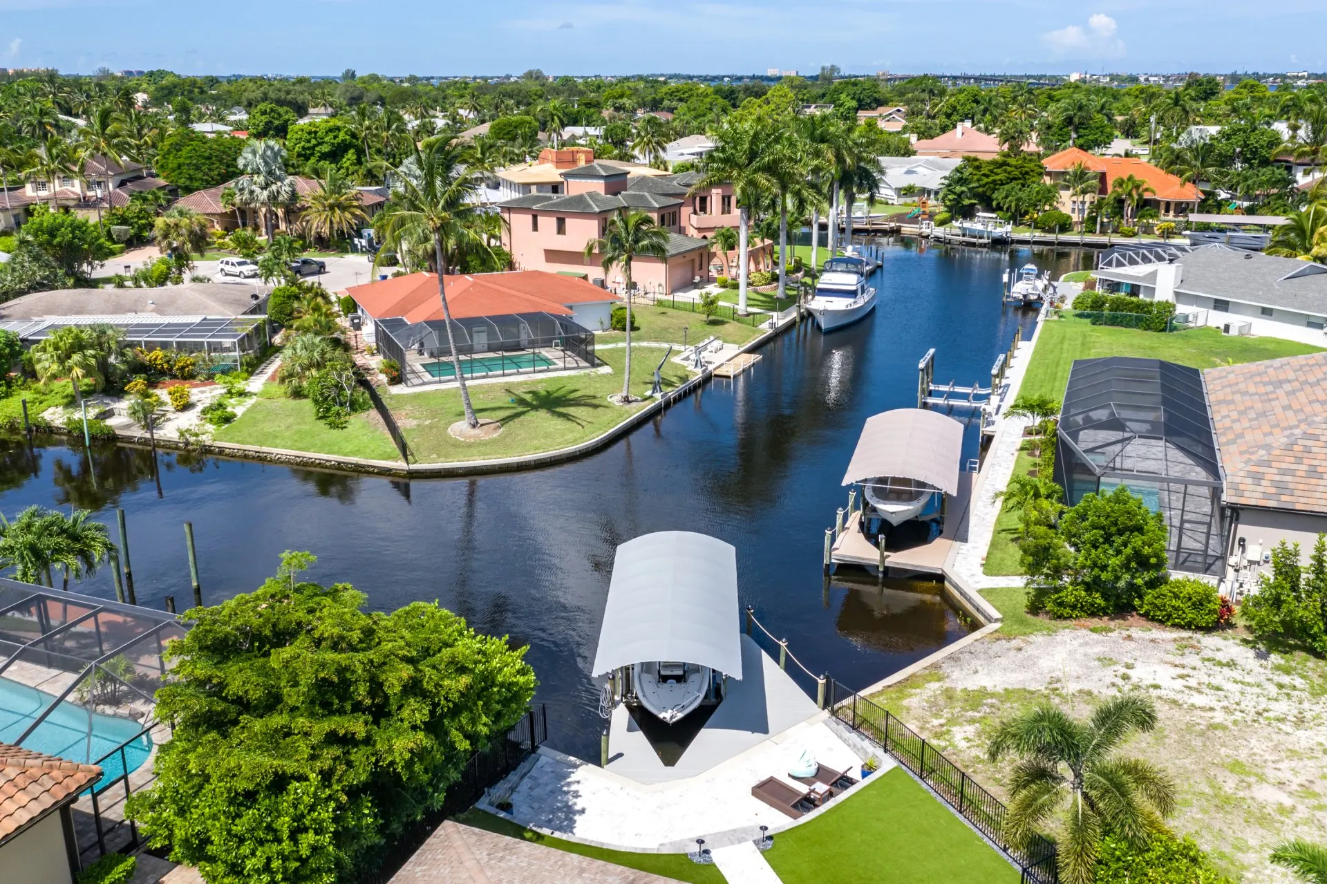 Aerial view of a canal with boat lifts, docks, and waterfront homes with lush landscaping.