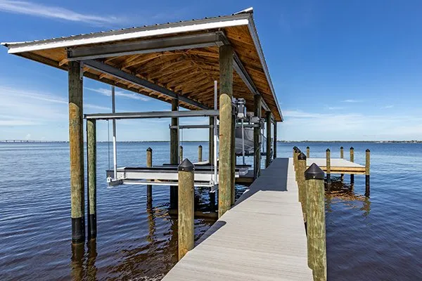 Covered dock with a boat lift extending over a calm waterfront under a clear blue sky.