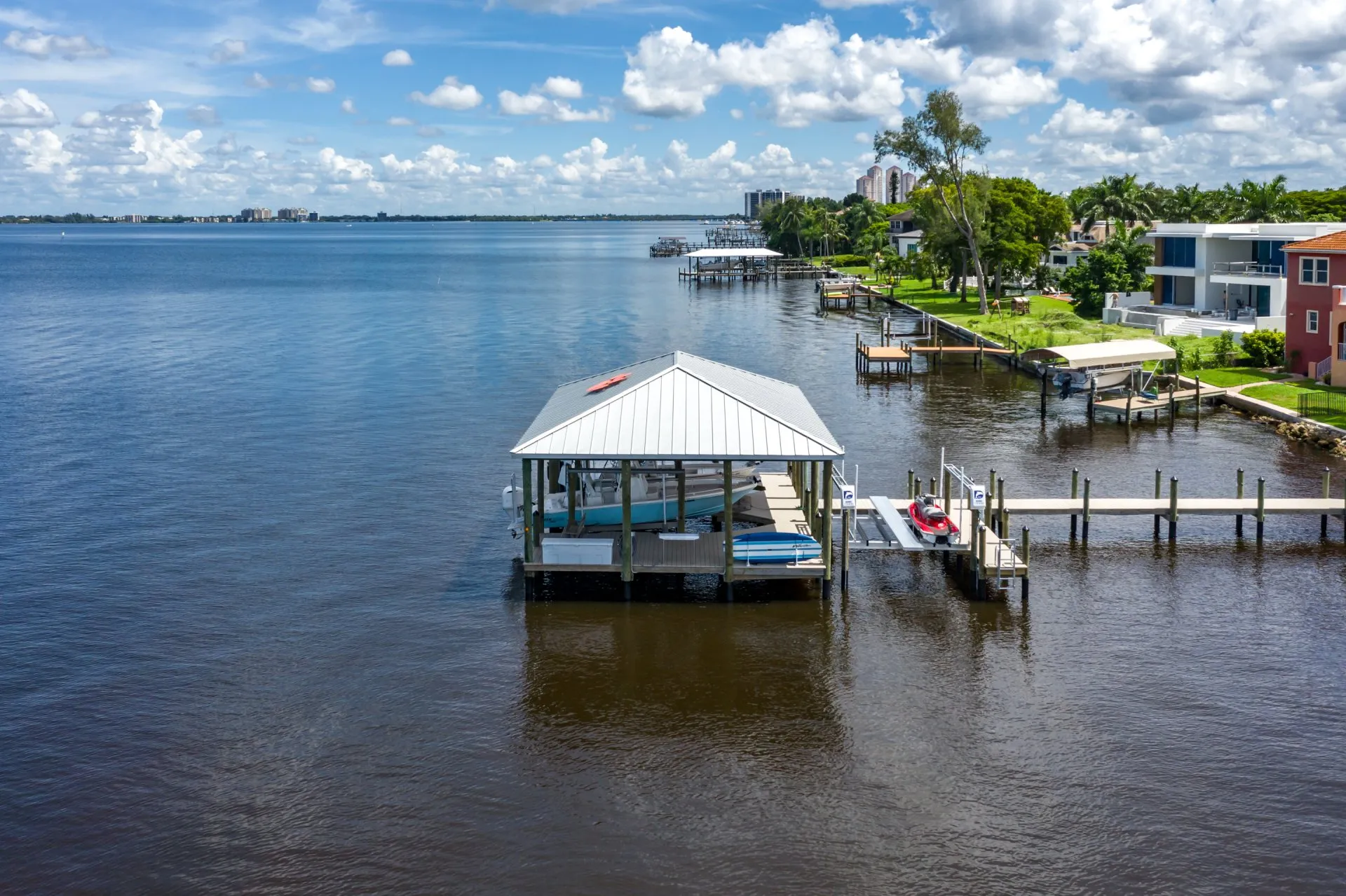 Covered dock with boats and a jet ski on a serene waterfront neighborhood.