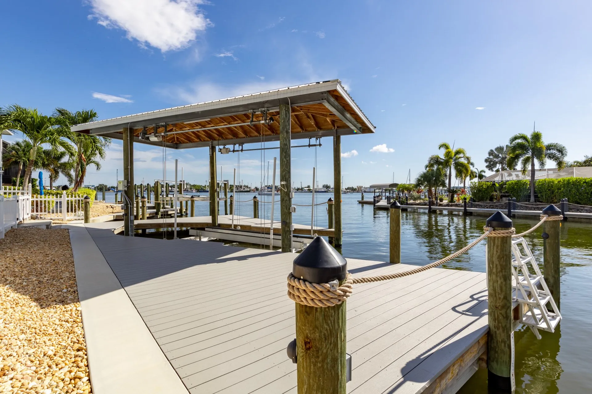 Covered dock with rope railings and a ladder overlooking a sunny waterfront.