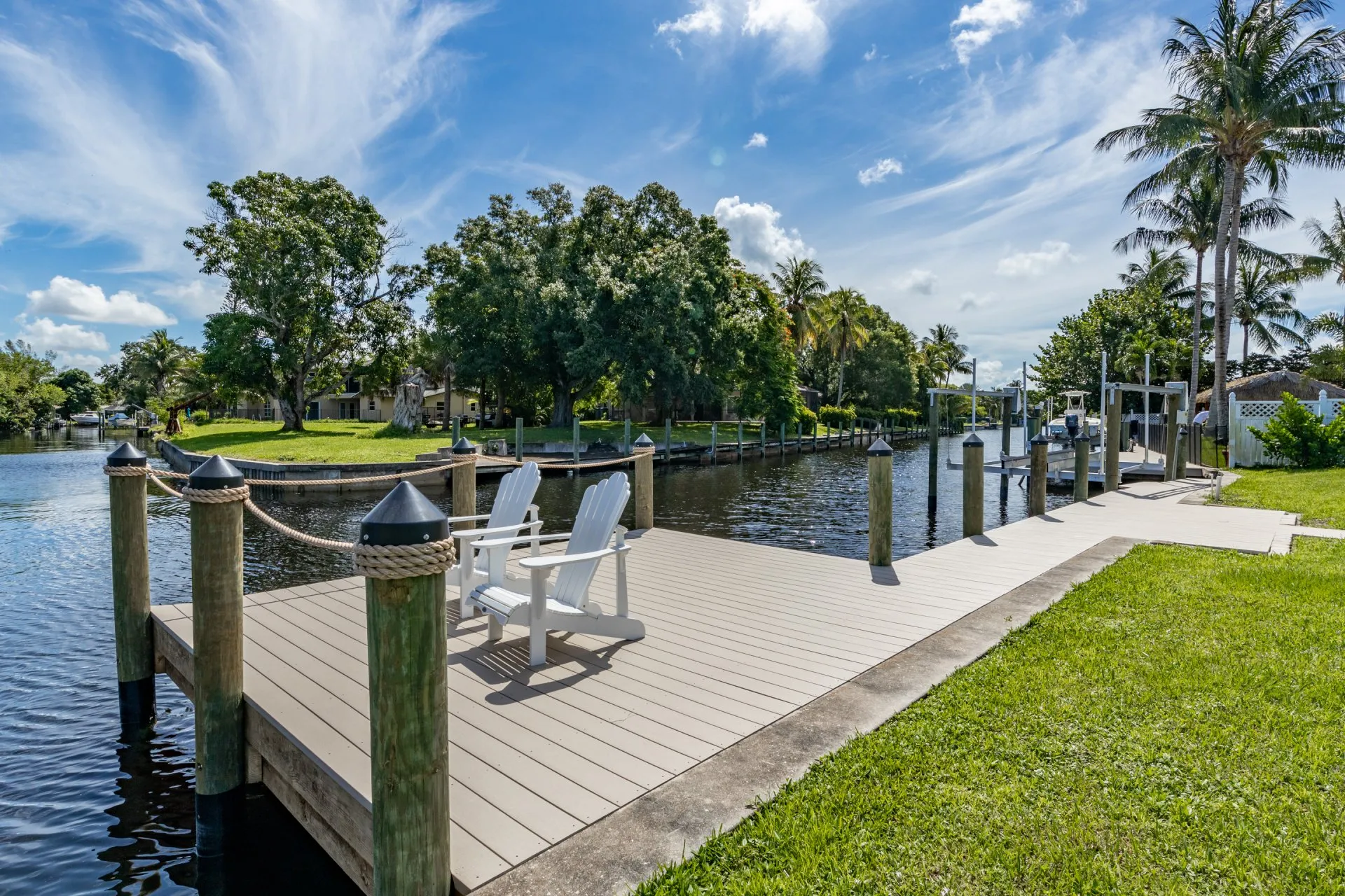 White chairs on a deck overlooking a peaceful canal lined with lush greenery and docked boats.