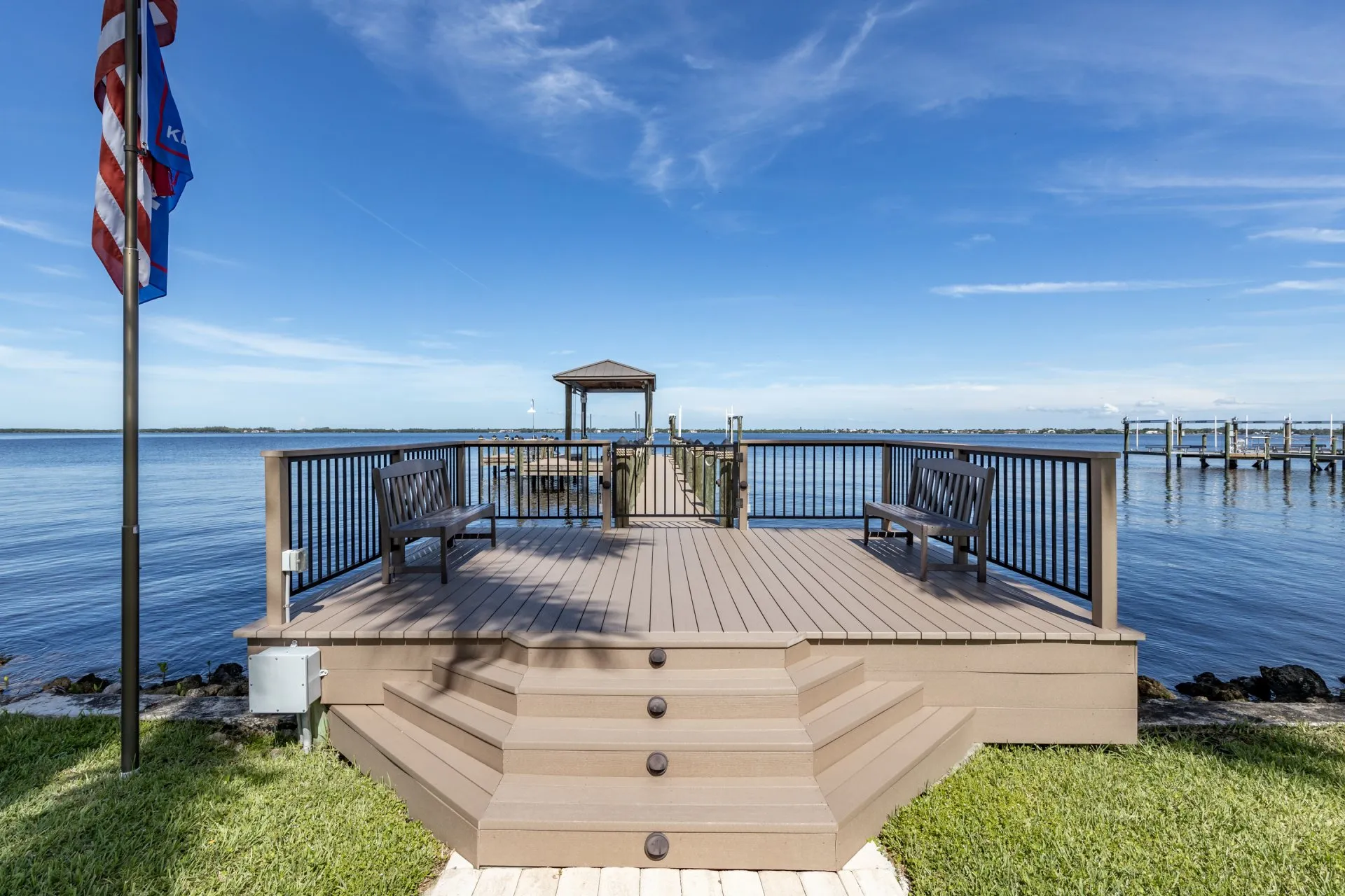 Waterfront deck with benches and a view of a dock extending over calm blue waters.