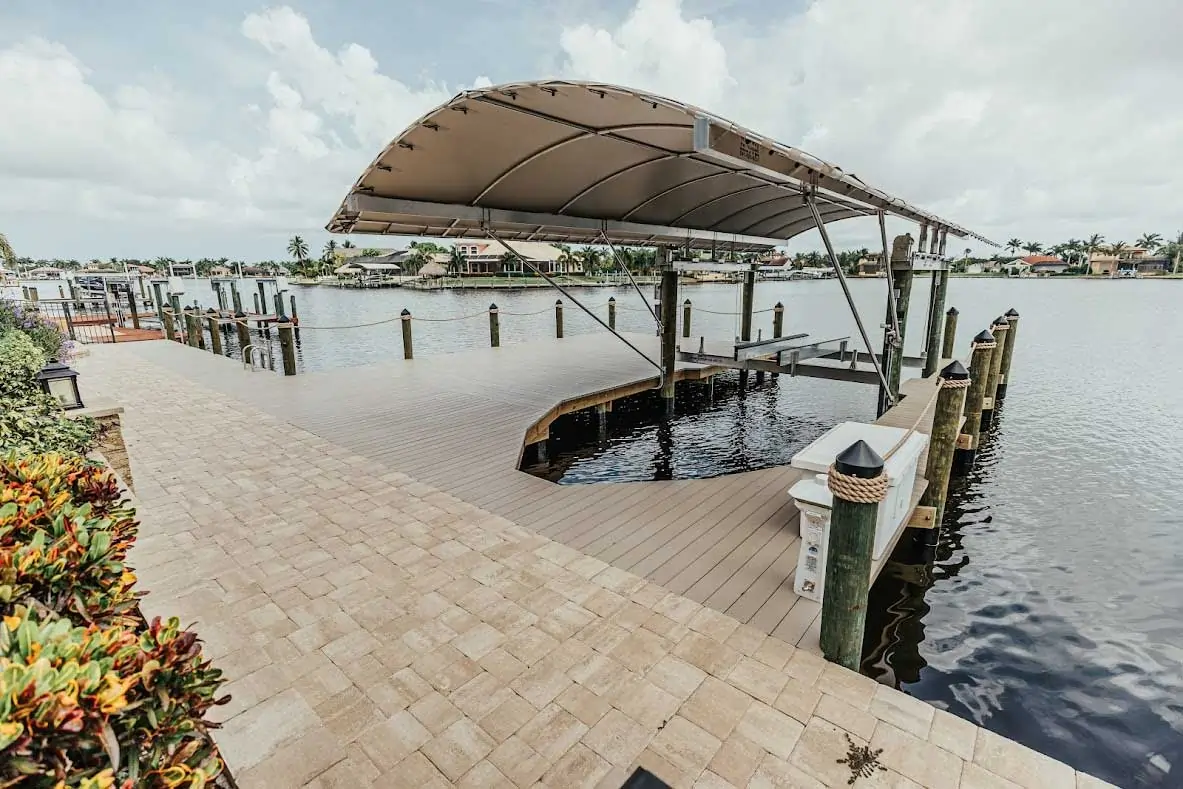 Dock with a curved boat lift cover, wooden posts, and water view on a cloudy day.