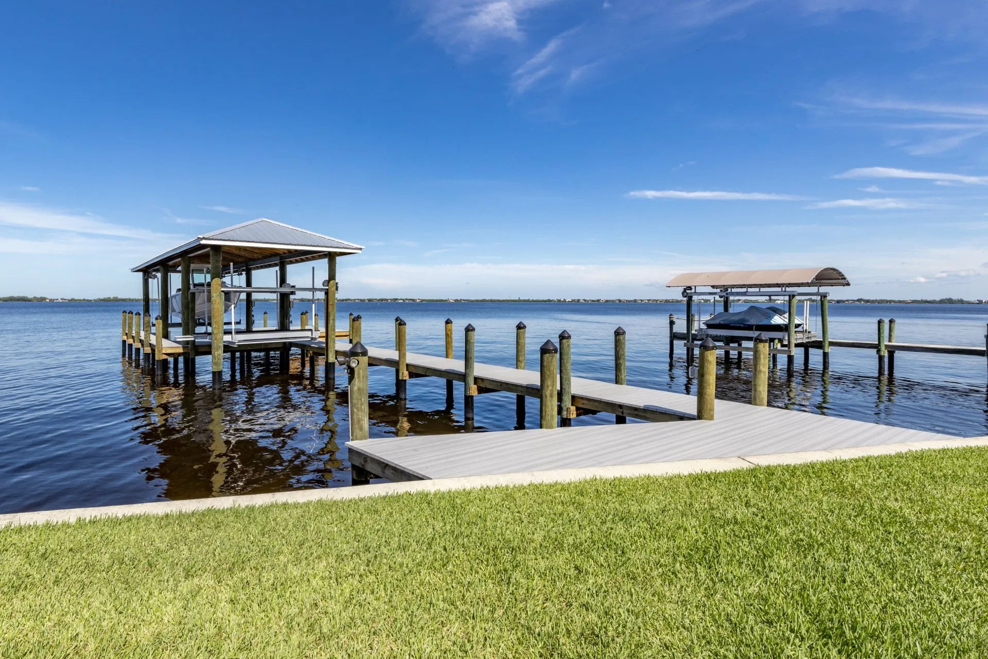 A scenic waterfront dock featuring a covered boat lift and adjacent uncovered lift.