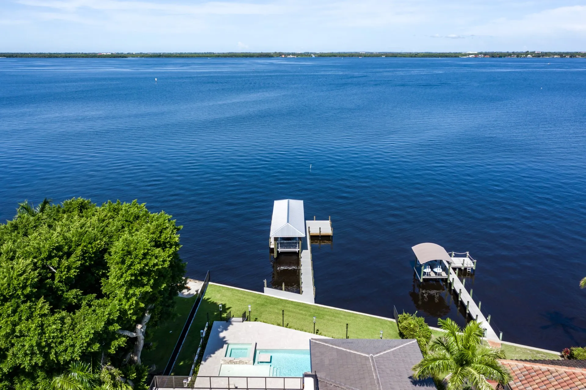 Aerial view of a waterfront property with a dock and covered boat lift surrounded by calm waters.