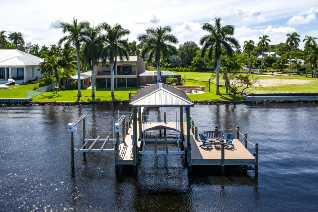 Waterfront dock with a pavilion and seating area overlooking lush green lawns and palm trees.