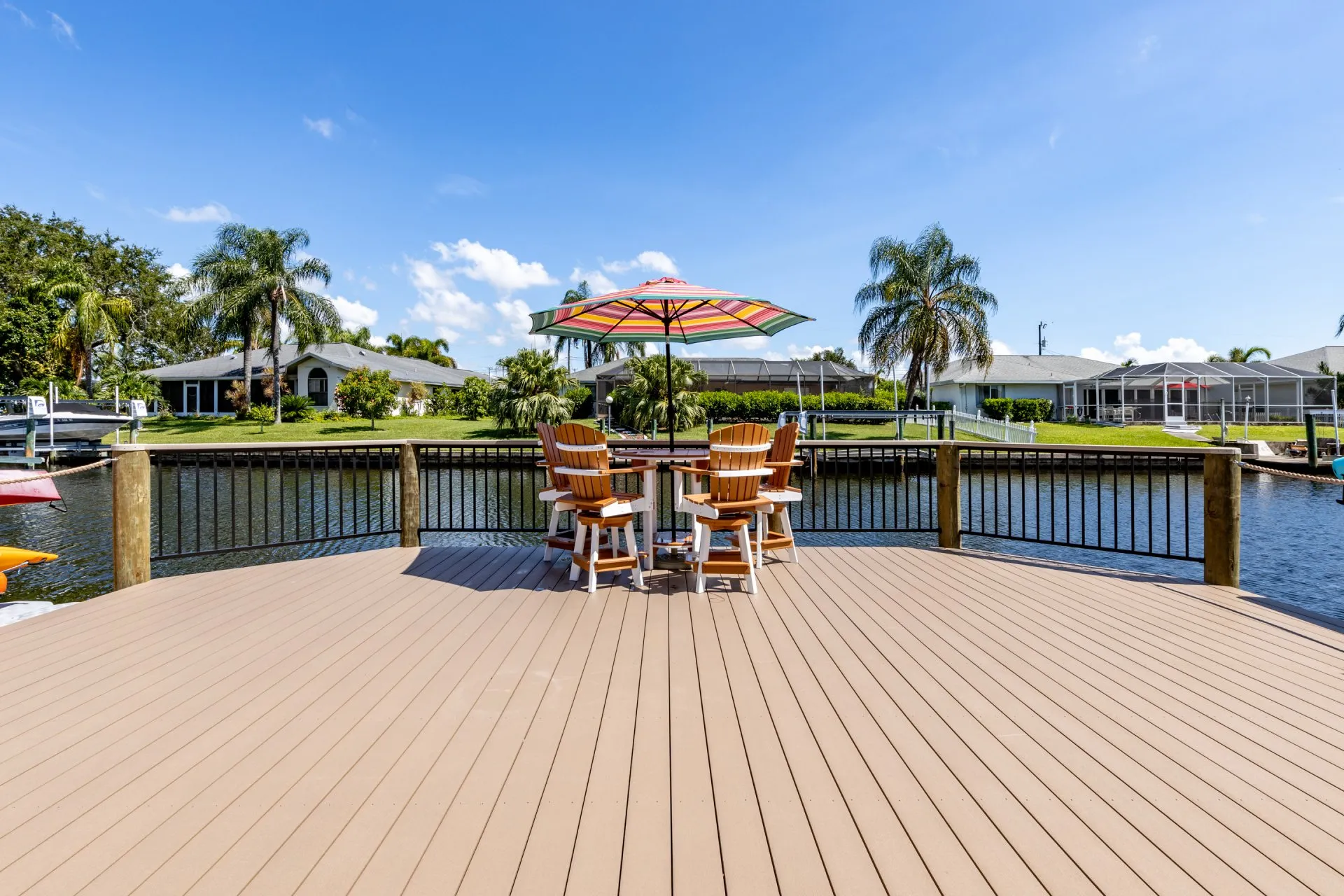 A waterfront dock with Adirondack chairs and a colorful umbrella, surrounded by a peaceful canal and lush greenery.