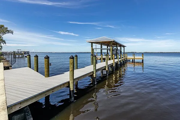 Waterfront dock with a covered boat lift and extended walkway over calm waters under a clear blue sky.